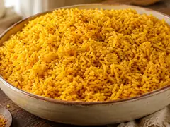 Arroz amarillo dorado anaranjado con motitas verdes de orégano y puntos de pimienta negra, servido en fuente de cerámica rústica sobre mesa de madera oscura, con una cuchara de madera con cúrcuma en polvo al costado