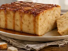 Budín de pan desmoldado con caramelo corriendo por los costados, con una porción cortada sobre plato de cerámica