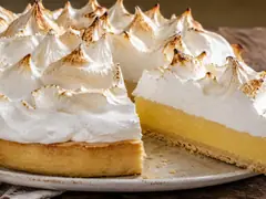 Lemon pie con una porcion cortada sobre plato de ceramica, mostrando las tres capas: base de masa, crema de limon amarilla y merengue italiano con los picos dorados al soplete